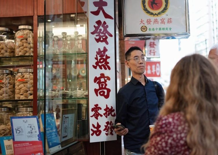 Gay-Friendly Hong Kong street food tour: Man in Hong Kong street with jars of food behind him. Gay travel advice in Hong Kong.