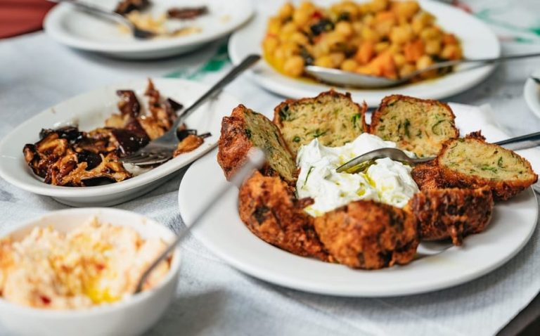 Athens foodie tour: Greek street food tastings. Plates of chickpea stew, fried zucchini balls with tzatziki, and mushroom dishes on a table.