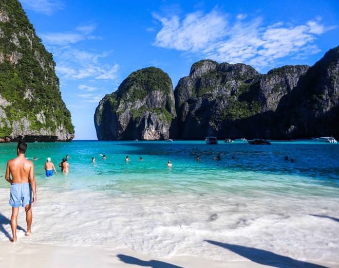 Gay-friendly Phi Phi Islands speedboat trip. Man on luxe beach, turquoise water, limestone cliffs. Beach lunch on gay travel adventure.