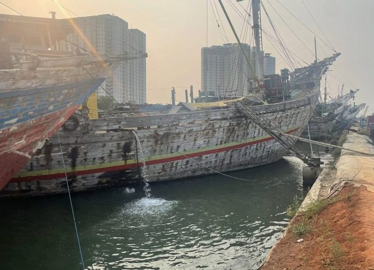 Jakarta highlights tour: Old wooden ships docked in harbor with city skyline. Gay travel advice for Indonesia.