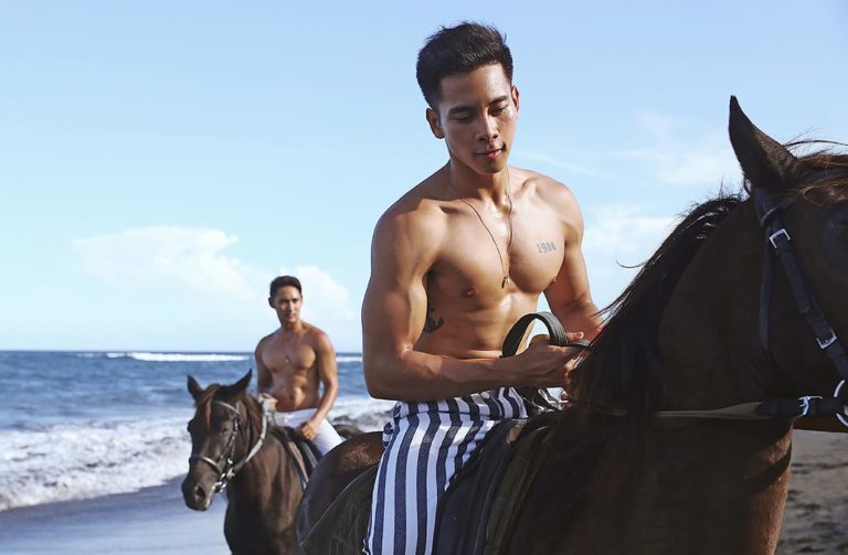 Shirtless gay men horseback riding on a Bali beach. Gay travel to Bali. Vacation goals. Gay Bali villa lifestyle.