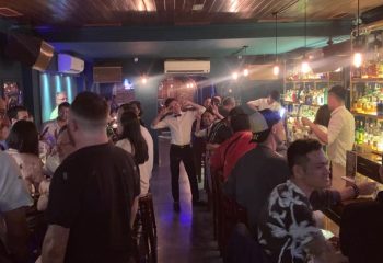 Busy gay bar in Hanoi. Bartender poses with peace signs. People drink at the bar. Gay travel advice for Vietnam.