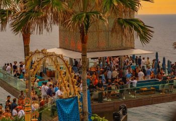 Glitterbox @ Hi Ibiza gay club. Outdoor party scene with palm trees, ocean views, and a lively crowd. Gay travel in Ibiza.