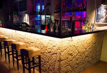 Grande Opera Frankfurt: Bar interior with stone facade, bar stools, illuminated bottles. Gay travel destination, vibrant nightlife.