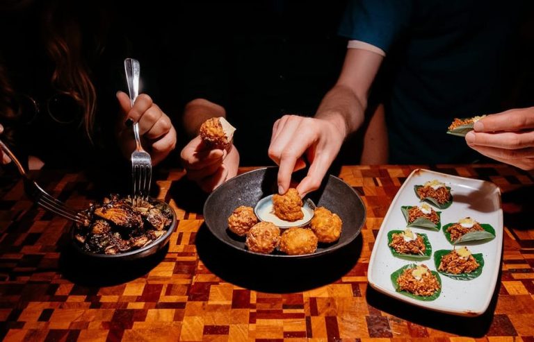 People enjoying a Guided Foodie Walking Tour through Melbourne's hot spots. Delicious appetizers on a wooden table. Gay travel.