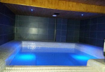 H2O Sauna, Benidorm. Interior view of the gay sauna's pool with blue lighting, tiled walls, and wooden ceiling, a relaxing space.