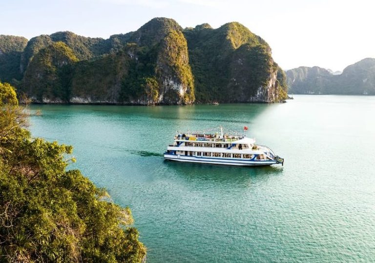 Halong Bay cruise ship sailing through turquoise waters. Explore Hanoi's natural beauty, a gay travel destination. Limestone karsts backdrop.