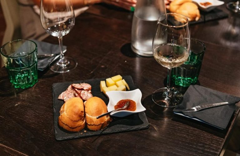 Fine Wines Private Tasting in Vienna: Table with wine glasses, bread, cheese, sausage, and jam on a slate board. Gay travel advice.