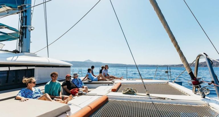 Gay travel: People on a luxury catamaran cruise in Santorini, enjoying open bar, meal, and stunning views of the Aegean Sea.