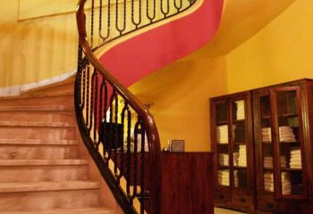 Ira Baths Athens: Interior view of a spiral staircase with wooden banister, leading up in a building in Athens. Gay travel advice.