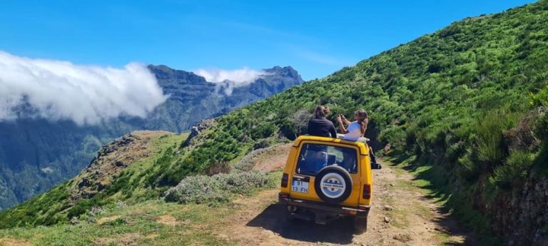 Madeira Jeep Safari: Two people on a yellow jeep roof, enjoying the views of Madeira's wild cliffs, pools, and peaks on a sunny day.