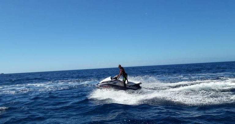 Gay man on a jetski, thrill ride in Puerto Rico de Gran Canaria. Water sports adventure on the waves. Blue sky, fun travel experience.