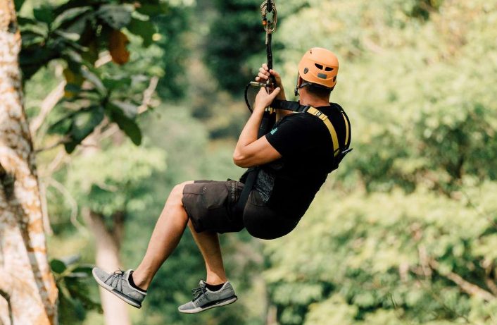 Gay traveler ziplining in Phuket's jungle paradise. Adventure tour with harness and helmet. Thrilling outdoor activity in Thailand.