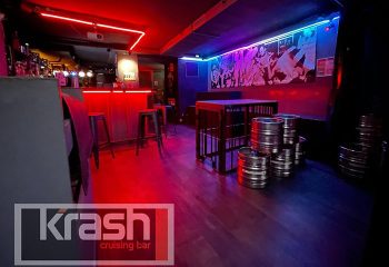 Krash Paris gay cruising bar interior. Red neon lights illuminate the bar area. Kegs are used as tables in the dimly lit space.