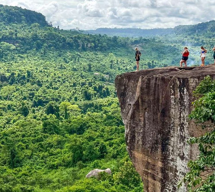 Kulen Mountain Beng Mealea Tonle Sap gay-friendly cultural adventure in Siem Reap. People on a cliff edge overlooking lush green jungle.