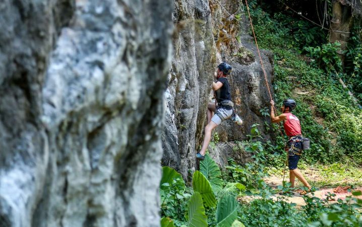Gay traveler rock climbing in Railay Beach, Thailand. Adventurous LGBT man on a climbing adventure. Lush greenery surrounds the limestone cliffs.