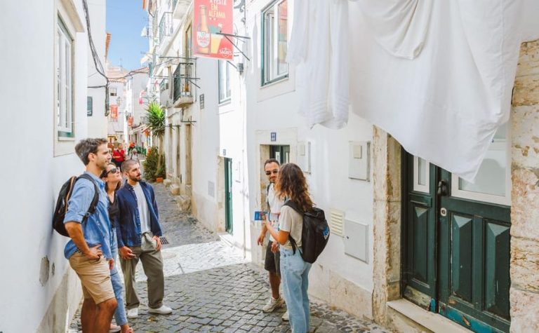 Lisbon Walking Tour: People explore Alfama's narrow street, white buildings, & hanging laundry. Rossio & Chiado vibes for gay men travel.