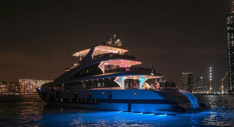 Night view of a luxe superyacht in Dubai. Live music, drinks, and wild views for gay travelers. Dubai skyline in the background.