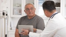 A photo of an older man with glasses speaking with his doctor in a clinic