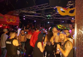 Mantrix Gay Club in Gran Canaria: A lively night scene with shirtless men and partygoers dancing under colorful lights and mask decorations.