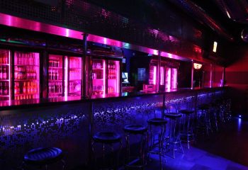 Mantrix Gay Club in Gran Canaria bar area. The bar is lit with pink and blue neon lights. Stools line the bar. Bottles are visible.