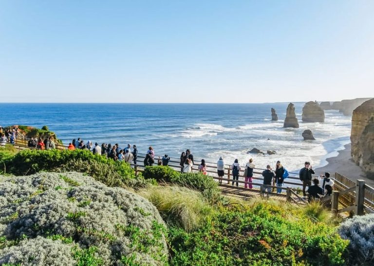 Great Ocean Road's Twelve Apostles, a must-see on a Melbourne day trip. Tourists admire the coastal rock formations & wildlife.