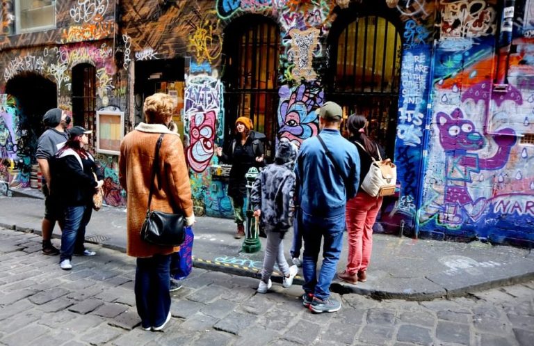 Melbourne Street Art Tour: Tourists explore hidden gems with a local artist amidst colorful graffiti. Gay travel adventure.