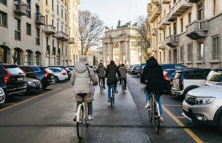 Milan unlocked: Cycling tour through hidden gems. People cycle down a Milan street towards Arco della Pace. Local secrets revealed.