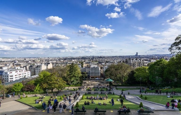Paris Montmartre view. People enjoy a sunny day in the park, with the city skyline in the background. A gay travel destination.