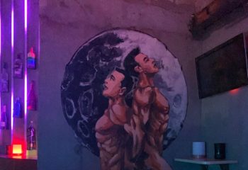 Shanghai gay bar: Moon Bar interior with a mural of two shirtless men in front of a moon. Bottles on a shelf with neon lights.
