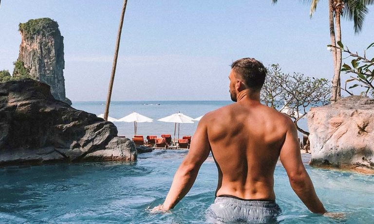 Gay man in Krabi, Thailand. Back view of a muscular man in a pool overlooking the beach, part of a popular holiday itinerary.