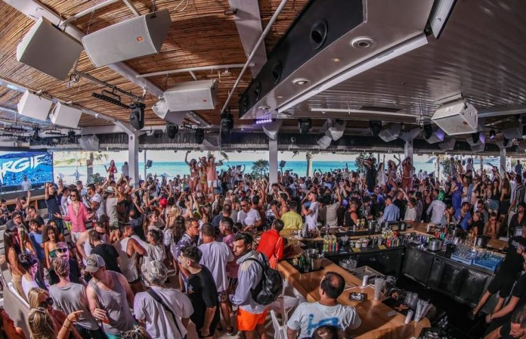 Mykonos beach club party scene. Energetic crowd, cocktails, and beats at a gay party. Beach crawl nightlife, travel advice.