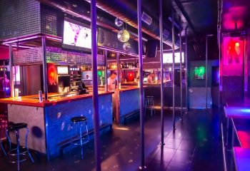 Interior of Mykonos Gay Club in Gran Canaria. Bar area, poles, disco balls, and colorful lighting create a vibrant atmosphere. Gay travel destination.
