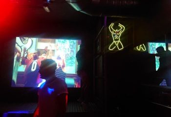 Mykonos Bar, Gran Canaria. Inside a gay club: neon man, screen with men dancing, dark atmosphere. Gay nightlife, travel advice.