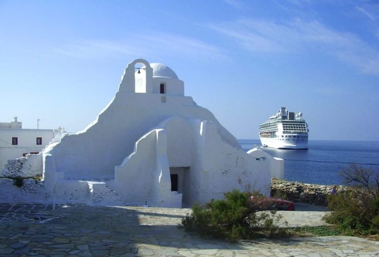 Mykonos guided tour: whitewashed monastery near beaches, cruise ship on sea. History and culture for gay travel.