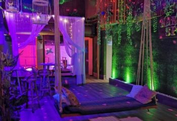 Madrid's NKD Spa gay cruise club interior. A swing bed, bar stools, and lush green wall create a sensual, inviting space. Gay travel.