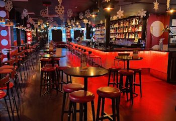 Pantibar gay bar interior in Dublin. Red lighting, stools, tables, and a fully stocked bar. A popular spot for gay men's travel.