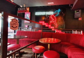 Pantibar Gay Bar, Dublin interior. Red seating, tables, and stools. Neon sign Absolut Pantibar. Toilets downstairs sign. Gay travel advice.