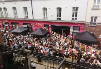 Crowd outside Pantibar, a popular gay bar in Dublin. Rainbow flags decorate the venue, celebrating LGBTQ+ pride. Gay travel destination.