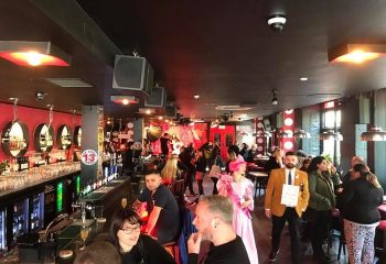 Interior of Pantibar, a popular gay bar in Dublin, Ireland. People are socializing near the bar and stage. Lively atmosphere.