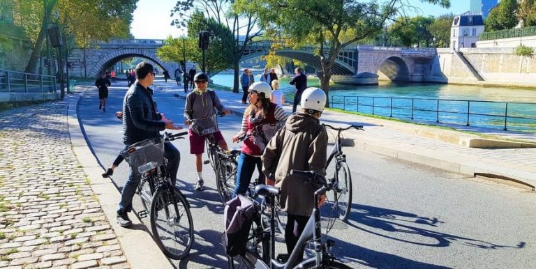 Paris city bike tour: A group pauses during their ride through history and culture along the Seine River, near a bridge. Gay-friendly hotspots tour.