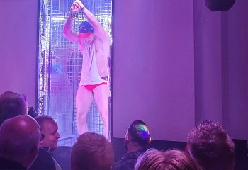 Paris RAIDD Bar: Go-go dancer in red briefs performs on stage. Gay nightlife scene in Paris. Audience members watch the show at RAIDD.
