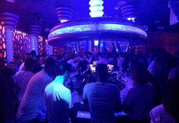 Crowded bar at Parthenon Gay Cruise Club in Torremolinos. Blue lighting illuminates patrons and the bar's unique décor. Gay travel hotspot.