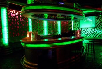 Interior of Parthenon Gay Cruise Club in Torremolinos. Bar area with green neon lights, zebra-striped wall, and modern design elements.