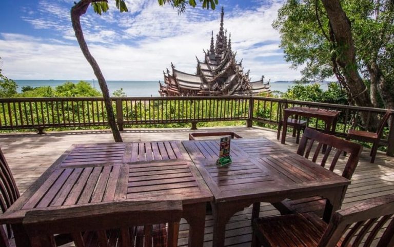 Pattaya, Thailand: Sanctuary of Truth view from a wooden deck with tables. Gay-friendly travel destination with culture, beach vibes, and views.