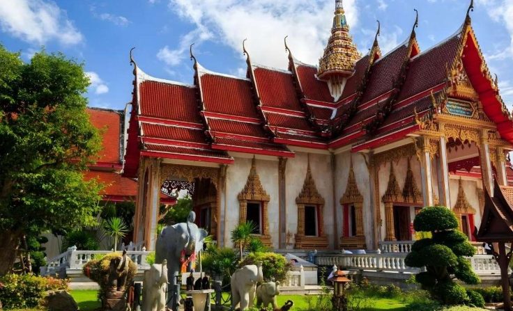 Phuket Full-Day Tour: Chillva Night Market vibes. Ornate Thai temple with red roofs, gold trim, and elephant statues. Gay travel in Thailand.
