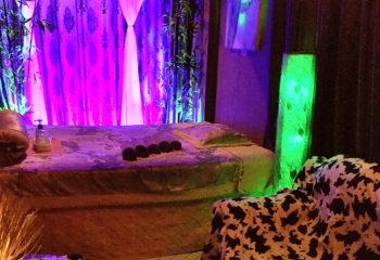 Polar Spa Hanoi room. Massage bed with rolled towels, pillows, and lotion. Green lamp and cow print chair. Gay travel advice.