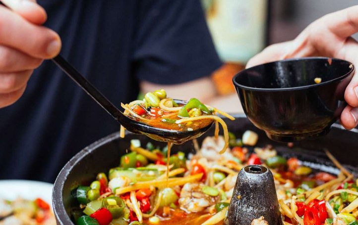 Private Food Tour: Local cuisine tasting. Person pouring sauce over a dish of noodles, peppers, and other vegetables.