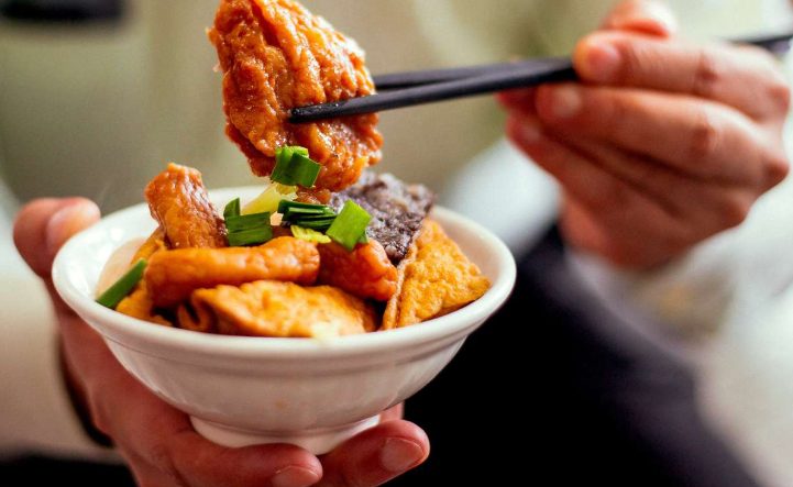 Taipei Food Tour: Hand holding a bowl of Taiwanese street food with chopsticks, featuring fried tofu, greens, and other local bites.