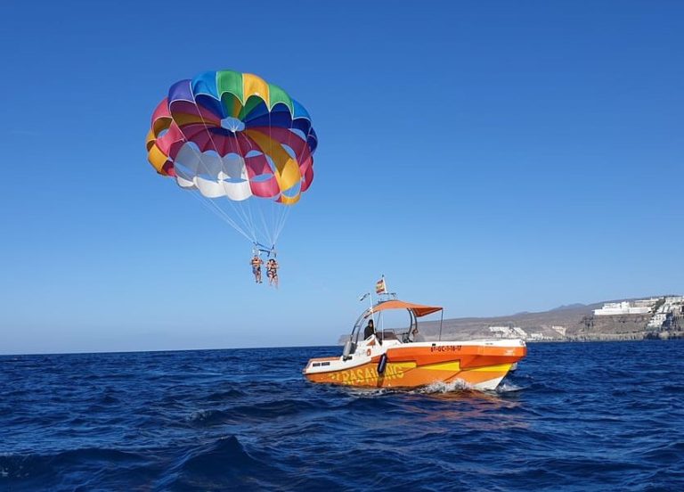 Gay-friendly Gran Canaria coastline: Parasailing adventure. Couple enjoys a colorful parachute ride above the ocean near Puerto Rico.